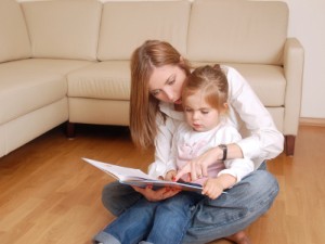 Young mom reading her little daughter on floor